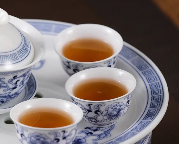 Blue-and-white porcelain tea set with three cups of amber tea on a matching tray.