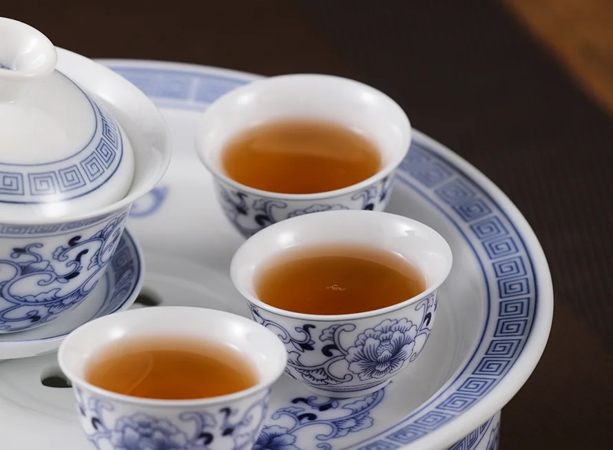 Blue-and-white porcelain tea set with three cups of amber tea on a matching tray.