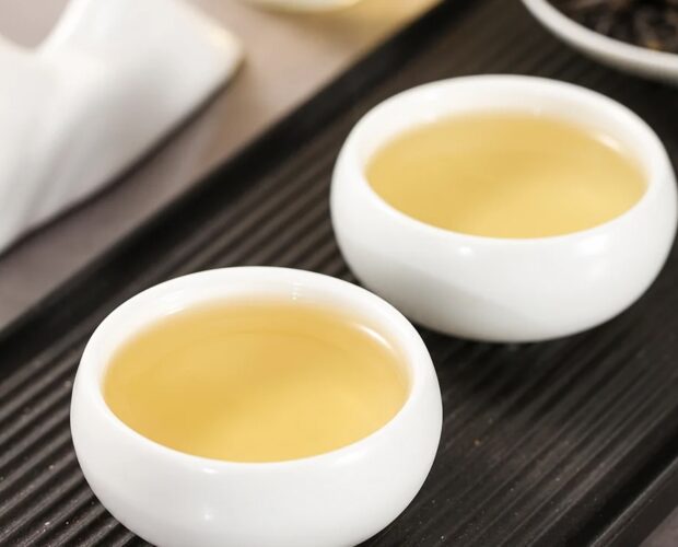 Golden yellow Phoenix Dan Cong Ya Shi Xiang oolong tea served in small white tasting cups on a dark tea tray