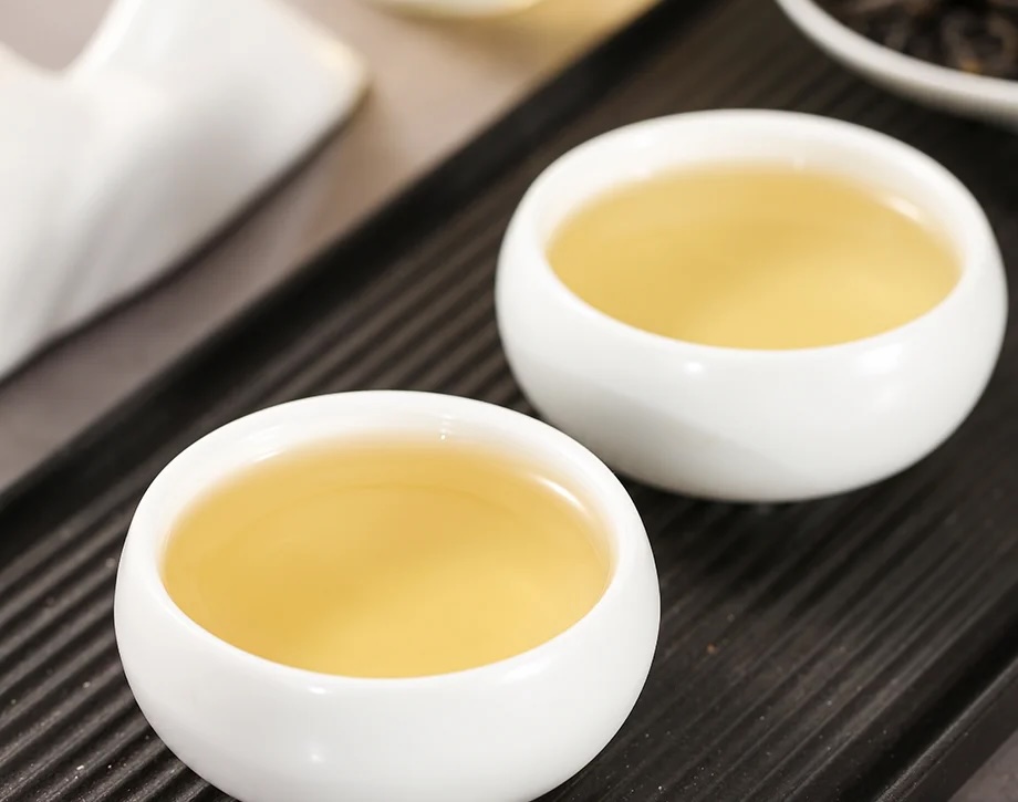 Golden yellow Phoenix Dan Cong Ya Shi Xiang oolong tea served in small white tasting cups on a dark tea tray