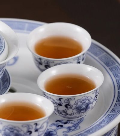 Blue-and-white porcelain tea set with three cups of amber tea on a matching tray.