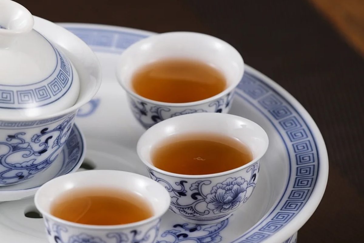 Blue-and-white porcelain tea set with three cups of amber tea on a matching tray.