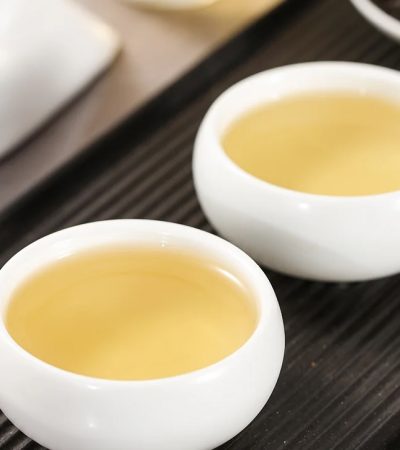 Golden yellow Phoenix Dan Cong Ya Shi Xiang oolong tea served in small white tasting cups on a dark tea tray