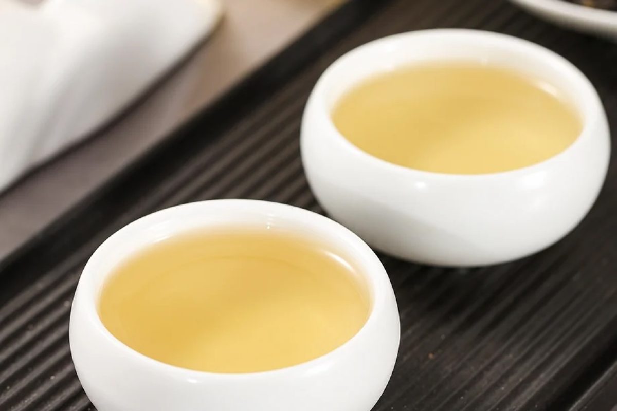 Golden yellow Phoenix Dan Cong Ya Shi Xiang oolong tea served in small white tasting cups on a dark tea tray